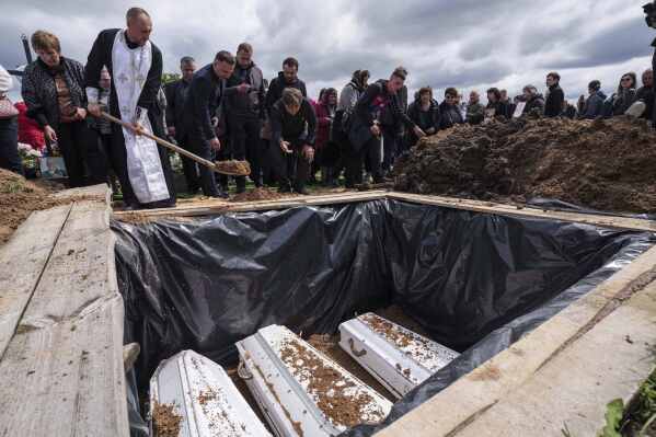 People throw earth into the grave during a funeral ceremony for Tamara Martyniuk, 8, Stanislav Martyniuk, 12, and Roman Martyniuk, 17, killed in a Russian strike on Sunday, in Korostyshiv, Zhytomyr region, Ukraine, Wednesday, May 28, 2025. (AP Photo/Evgeniy Maloletka)
