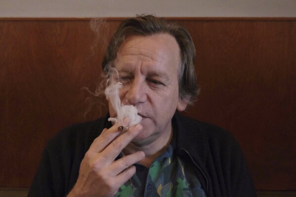 Derrick Bergman, chairman of the Union for the Abolition of Cannabis Prohibition, smokes a marijuana cigarette in coffeeshop De Baron in Breda, Netherlands, on Friday, Dec. 15, 2023. Bergman was at the coffeeshop to mark the start of a new experiment with legally grown weed going on sale in two Dutch cities. (AP Photo/Mike Corder)