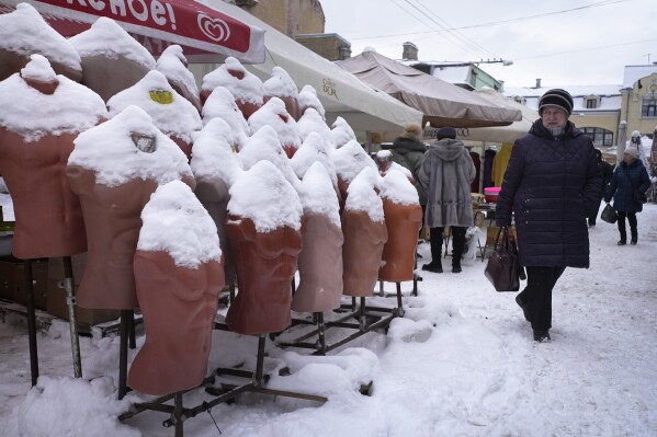 A woman walks past mannequins covered in snow after a snowfall at a street market in St. Petersburg, Russia, Friday, Feb. 14, 2025. (AP Photo/Dmitri Lovetsky)