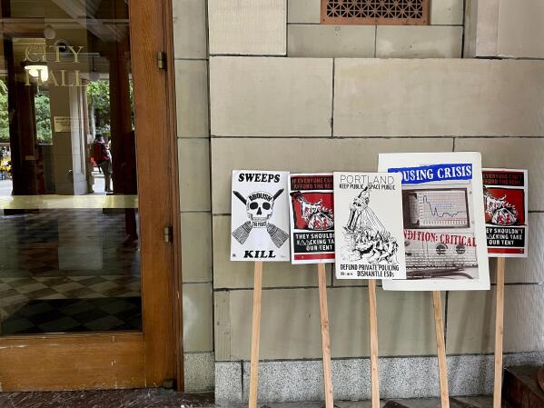 FILE - Protest signs condemning a measure in Portland City Council that would ban homeless camps during the daytime in most public places are lined up next to one of the doors of City Hall in Portland, Ore., May 31, 2023. Portland's city council voted Wednesday to pass an ordinance prohibiting camping during daytime hours in most public places as it, along with other U.S. cities, struggles to address a longtime homelessness crisis. (AP Photo/Claire Rush, File)