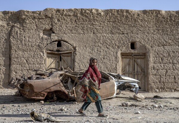 A girl walks past a destroyed car in a village in a remote region of Afghanistan, on Saturday, Feb. 25, 2023. (AP Photo/Ebrahim Noroozi)