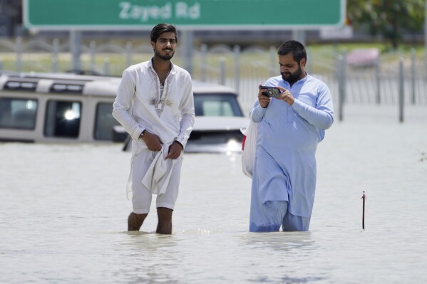 Two men walk through floodwater in Dubai, United Arab Emirates, Wednesday, April 17, 2024. The desert nation of the United Arab Emirates attempted to dry out Wednesday from the heaviest rain ever recorded there after a deluge flooded out Dubai International Airport, disrupting the world's busiest airfield for international travel. (AP Photo/Jon Gambrell)