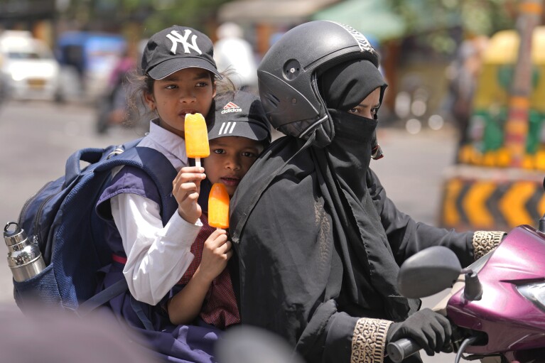 Schoolchildren eat ice lollies sitting on a scooter on a hot summer day in Lucknow, India, Friday, May 3, 2024. (Ǻ Photo/Rajesh Kumar Singh)
