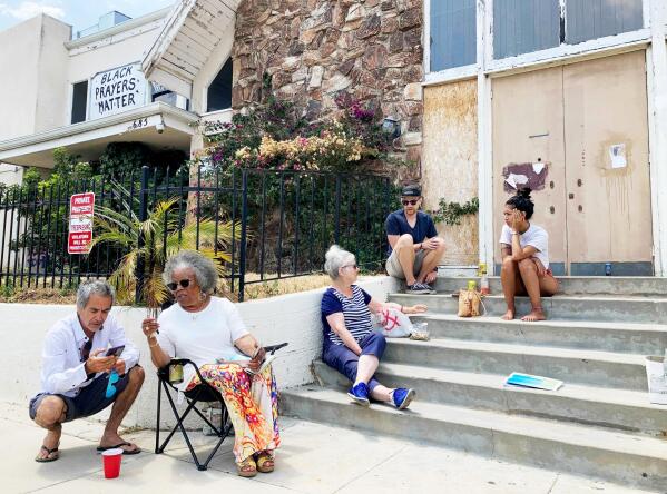 From right, Stephanie Serra and her husband Chase Cole sit at the top of the steps of First Baptist Church of Venice while talking to Ingrid Mueller, center, on Sunday, July 11, 2021, in Los Angeles as Naomi Nightingale, left, speaks with a visitor from her lawn chair before returning to the conversation. The group meets here every other Sunday to discuss ways to preserve the abandoned church building.  (Alejandra Molina/RNS via AP)