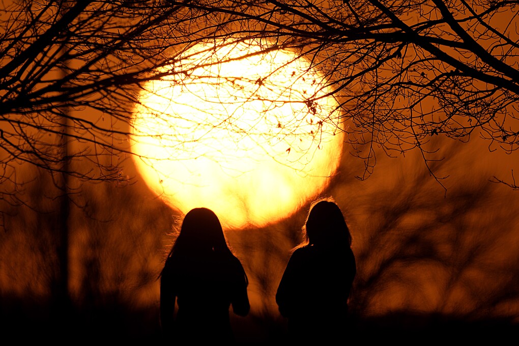 FILE - People watch the sunset at a park on an unseasonably warm day, Feb. 25, 2024, in Kansas City, Mo. A new study says climate change will reduce future global income by about 19% in the next 25 years compared to a fictional world that’s not warming. (AP Photo/Charlie Riedel, File)