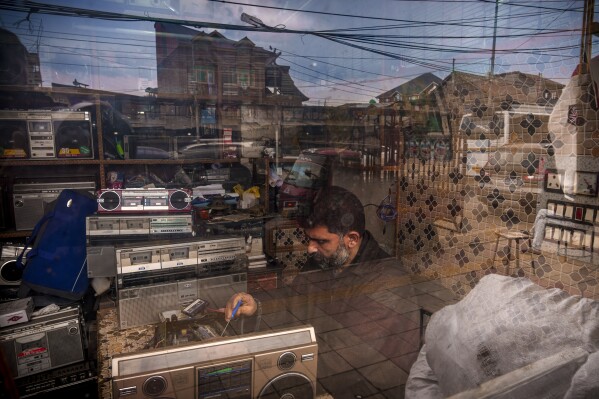 Self-taught tape recorder mechanic Mohammad Ashraf Matoo is seen through a glass window as he repairs a tape recorder at his shop in Srinagar, Indian controlled Kashmir, Tuesday, Feb. 11, 2025. (AP Photo/Dar Yasin)