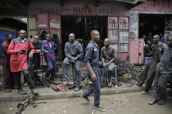 Workers gather as they wait for customers outside a secondhand car parts shop in the industrial area of the capital Nairobi, Kenya, Friday, Oct. 7, 2022. In a gritty neighborhood of Nairobi known for fixing cars and selling auto parts, businesses are struggling and customers are unhappy. (AP Photo/Brian Inganga)