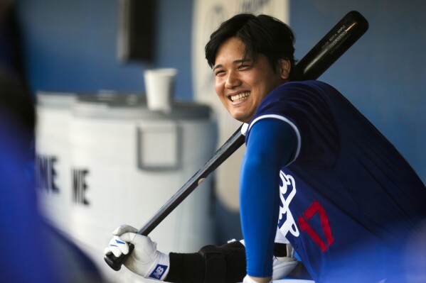 FILE- Los Angeles Dodgers designated hitter Shohei Ohtani smiles in the dugout before a spring training baseball game against the Los Angeles Angels in Phoenix, Tuesday, March 5, 2024. (AP Photo/Ashley Landis, File)