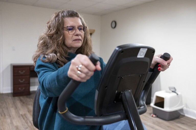 Donna Cooper shows her exercise bike at her home in Front Royal, Va., on Friday, March 1, 2024. Generally, Cooper maintains her fitness regimen with walks with friends. Once she's done with her Wegovy injections, Cooper said she’ll just continue with a strict diet and exercise plan. (AP Photo/Amanda Andrade-Rhoades)