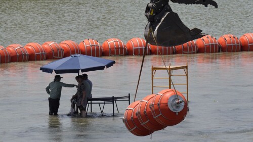 Workers take a break from deploying large buoys to be used as a border barrier along the banks of the Rio Grande in Eagle Pass, Texas, Wednesday, July 12, 2023. The floating barrier is being deployed in an effort to block migrants from entering Texas from Mexico. (AP Photo/Eric Gay)