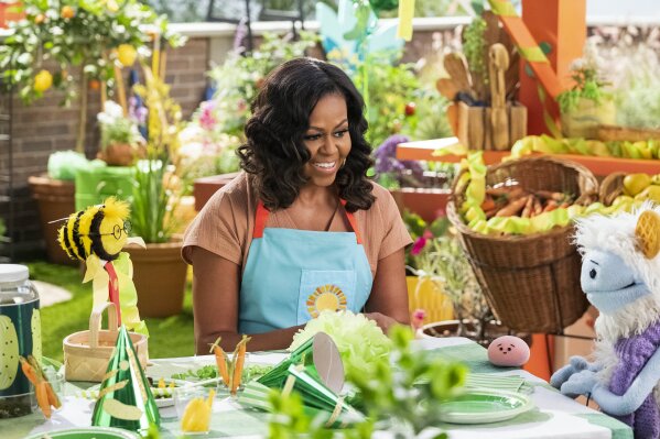 This image released by Netflix shows former first lady Michelle Obama with Busy, a bee puppet, left, Mochi, a pink round puppet, and Waffles, a furry puppet with waffle ears on the set of the children's series "Waffles + Mochi." Obama is launching the new Netflix children’s food show on March 16. (Adam Rose/Netflix via AP)