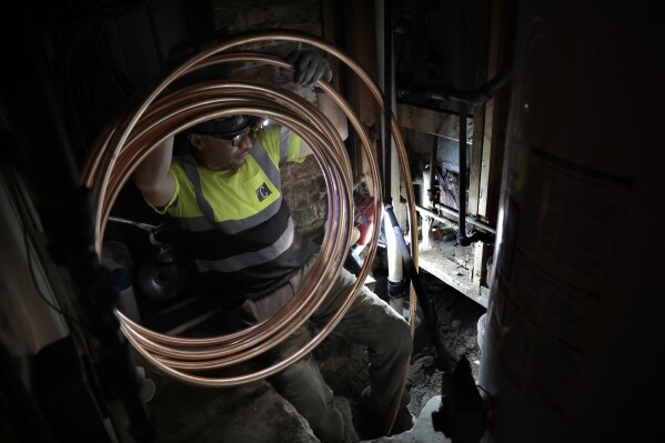 A laborer holds onto a coiled copper pipe as it is pulled from the home, under the ground and out to the street for connection to the water main during lead service replacement on April 10, 2023, in Chicago. Lead pipes that carry drinking water are a major source of exposure to the metal and the damage is usually permanent. (Antonio Perez/Chicago Tribune via AP)