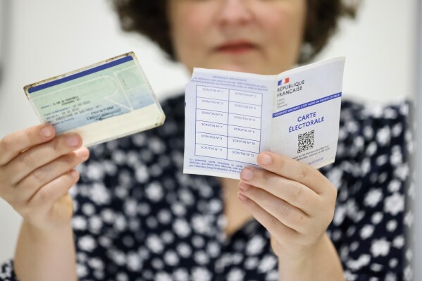 A voting assistant checks the voting card, right, and an identity card in Strasbourg, eastern France, Sunday, June 30, 2024. (AP Photo/Jean-Francois Badias)