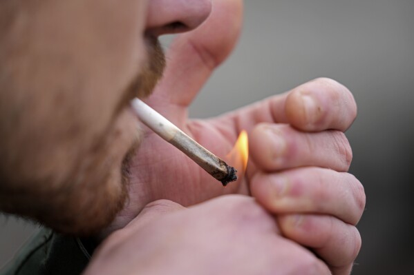FILE - A man smokes cannabis in front of the Cathedral in Cologne, Germany, at a public consumption event at the start of a new law on Monday, April 1, 2024. Austria will step up police checks near its border with Germany after its neighbor legalized the possession of small amounts of cannabis for recreational use, the country's top security official said Tuesday, April 2, 2024.(AP Photo/Martin Meissner, File)