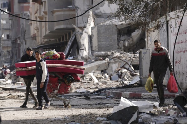 Palestinians walk through destruction by the Israeli bombardment in the Nusseirat refugee camp in Gaza Strip, Tuesday, Jan. 16, 2024. (AP Photo/Adel Hana)