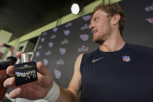 Tennessee Titans quarterback Will Levis, right, holds a bottle of his new cologne after a news conference following an NFL joint football training camp practice with the Seattle Seahawks, Wednesday, Aug. 14, 2024, in Nashville, Tenn. (AP Photo/George Walker IV)