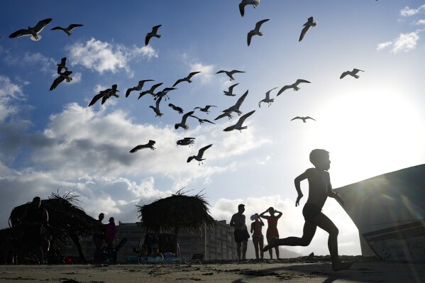 A youngster runs as others watch the seagulls on Panty Beach during the holiday break in La Guaira, Venezuela, Wednesday, Jan. 3, 2024. (AP Photo/Matias Delacroix)
