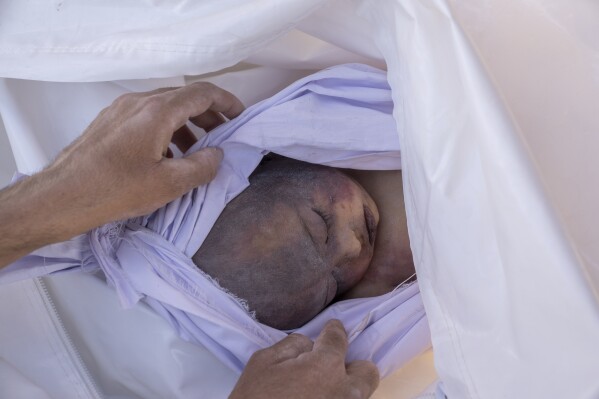 EDS NOTE: GRAPHIC CONTENT - An Afghan man looks at the face of his child who was killed by an earthquake, before the burial, in a village in Zenda Jan district in Herat province, western of Afghanistan, Monday, Oct. 9, 2023. Saturday's deadly earthquake killed and injured thousands when it leveled an untold number of homes in Herat province. (AP Photo/Ebrahim Noroozi)