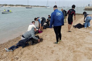 FILE - Migrants are rescued by locals on the shore of a beach, close to the southwestern city of Cádiz, Spain, Thursday, Nov. 30, 2023. Spanish police say they've arrested three people for the deaths of five migrants who were forced to jump off the boat they were traveling in with dozens of other migrants. A police statement on Monday, March 18, 2024 said the five died late last November off the southern coast of Cádiz. (AP Photo/Jorge Gonzalez Casares, File)