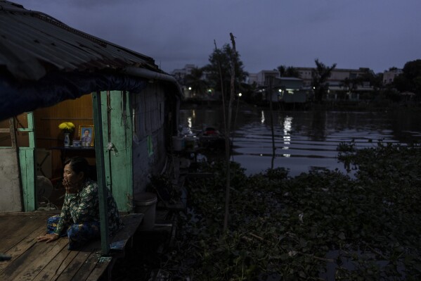 Nguyen Thi Thuy, a vendor selling steamed buns on a floating market to make ends meet, sits on her houseboat along a river prone to frequent flooding in Can Tho, Vietnam, Tuesday, Jan. 16, 2024. Unable to afford rent on land, the small family has lived on a small houseboat ever since. (AP Photo/Jae C. Hong)
