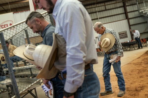 Rancher GC Ellis, right, bows his head in prayer before a cattle auction in Gainesville, Texas, Friday, April 21, 2023. Ellis built his ranch in 1982 on 450 acres. It's where his children roamed through the pastures, creeks and hardwood forests as the family added land and cattle over the years. It's now grown to 3,000 acres and his daughter, Meredith, now runs the day-to-day operations. (AP Photo/David Goldman)
