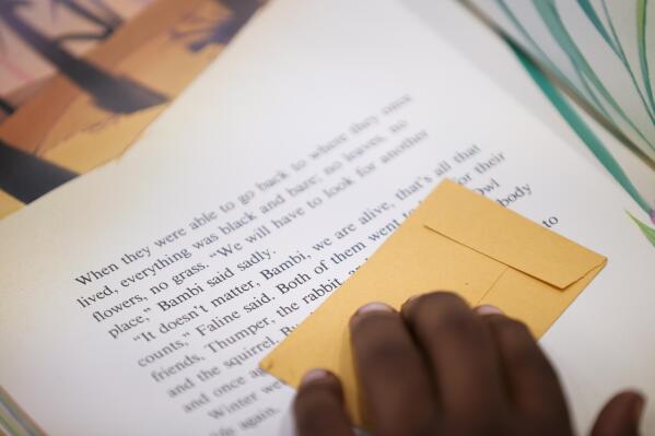 Michael Crowder, 11, follows along with a bookmark as he reads during an after-school literacy program in Atlanta on Thursday, April 6, 2023. When he's not in school, Michael has been dropping by his apartment complex’s community center most afternoons to read books to the staff, who encourage the activity with pizza parties. His report cards show improvement. His parents have noticed his growth. (AP Photo/Alex Slitz)