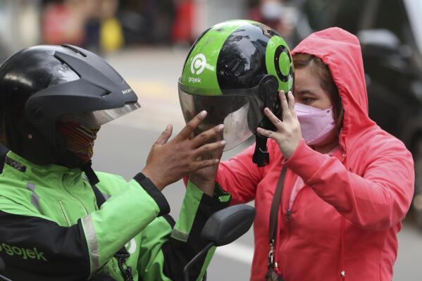 A Gojek driver gives a helmets to a customer in Jakarta, Indonesia, Monday, May 17, 2021. Indonesian ride hailing company Gojek and e-commerce firm Tokopedia said Monday that they are merging, in the largest ever deal in the country's history. (AP Photo/Achmad Ibrahim)