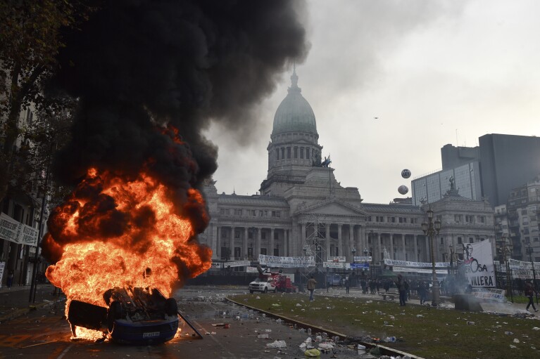 2024 年 6 月 12 日星期三，在阿根廷布宜诺斯艾利斯国会外，议员们正在辩论阿根廷总统哈维尔·米莱提出的改革法案，警方与反政府抗议者发生冲突，一辆汽车燃烧。（美联社照片/古斯塔沃·加雷洛）