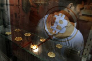 FILE- In this Dec. 8, 2017, file photo, a man uses a Bitcoin ATM in Hong Kong. Digital currency exchange Coinbase is looking to become a publicly traded company, a move being hailed by some as a start to helping cryptocurrency gain more mainstream acceptance. Coinbase Global Inc., in a filing with the Securities and Exchange Commission, is seeking a direct listing, which would allow company workers and investors to convert their stakes into stock. (AP Photo/Kin Cheung, File)