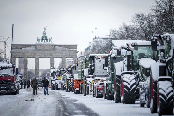 FILE - Farmers with tractors protest at the Brandenburg Gate in Berlin, Germany, Tuesday, January 16, 2024. Snow-covered tractors lined up outside the Brandenburg Gate and nighttime protests in Romania marked by bright national flags mark widespread peasant protests. Moving around Europe.  (Kay Nietfeld/DPA, via AP, File)