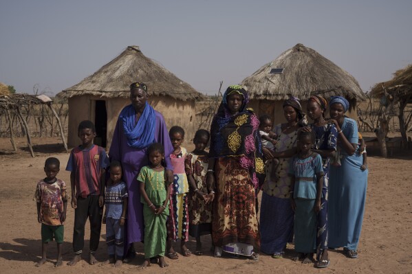 Mamadou Samba Sow, 63, center left, and his wife, Dieynaba Toure, 46, center right, stand for a picture with their family at their compound in the village of Anndiare, in the Matam region of Senegal, Thursday, April 13, 2023. In the Sahel region — where the United Nations estimates 65% of meat and 70% of milk sold at local markets come from pastoralists — the head of the Association for Promoting Livestock Farming in the Sahel and Savannah suggests people put their children in school and diversify incomes. (AP Photo/Leo Correa)