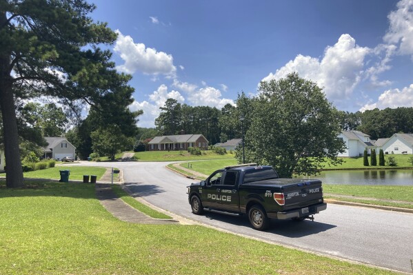 A police vehicle stands guard in the Dogwood Lakes neighborhood in Hampton, Ga., on Sunday, July 16, 2023. Police say a man who lived in the brick house in the background shot and killed four people in the neighborhood on Saturday, July 15. (AP Photo/Jeff Amy)