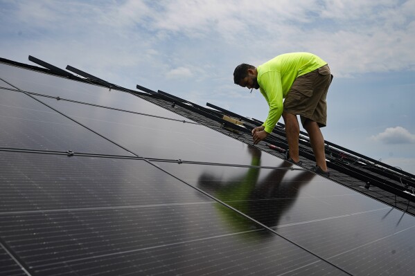 FILE - Nicholas Hartnett, owner of Pure Power Solar, secures solar panel on the roof of a home in Frankfort, Ky., Monday, July 17, 2023. In campaigns for Congress and for governor around the country, candidates are talking about how green the grid should be (AP Photo/Michael Conroy, File)
