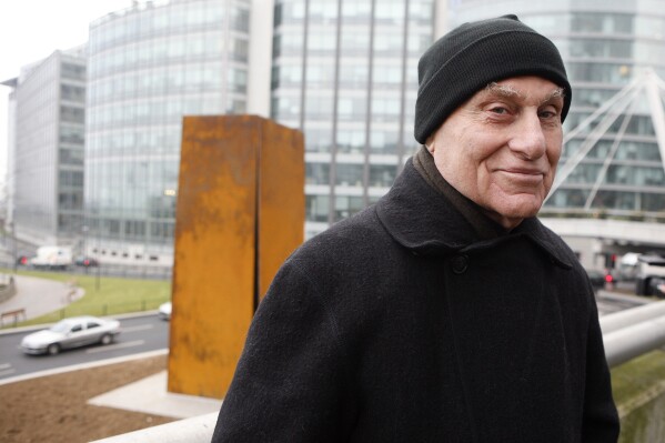 FILE - Famed American sculptor Richard Serra poses in front of "Slat," a 1984 steel sculpture, after its reinstallation in La Defense, west of Paris, Dec. 15, 2008. Serra, known for turning curving walls of rusting steel and other malleable materials into large-scale pieces of outdoor artwork that are now dotted across the world, died Tuesday, March 26, 2024, at his home in Long Island, N.Y. He was 85. (AP Photo/Jacques Brinon, File)