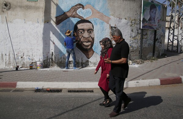 FILE - Palestinians people walk past an artist painting a mural of George Floyd, a black American who died after being restrained by police officers, in Gaza City, Tuesday, June 16, 2020. (AP Photo/Hatem Moussa, File)