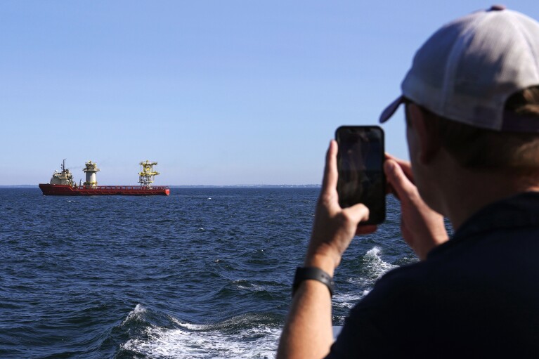 Aaron Smith, President and CEO of the Offshore Marine Service Association, photographs ships installing portions of a wind farm, Tuesday, July 11, 2023, off the coast of Rhode Island. (AP Photo/Charles Krupa)