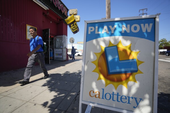 A man walks by a sign for the lottery in front of a market Tuesday, July 18, 2023, in San Diego. The Powerball jackpot rose yet again to an estimated $1 billion after no winning ticket was sold for the latest drawing. (AP Photo/Gregory Bull)