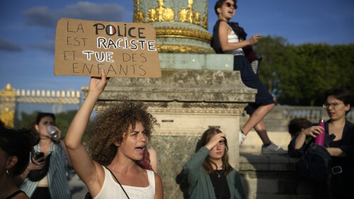 A woman holds a placard reading "Police are racist and kill children" during a protest in Paris, France, Friday, June 30, 2023. French President Emmanuel Macron urged parents Friday to keep teenagers at home and proposed restrictions on social media to quell rioting spreading across France over the fatal police shooting of a 17-year-old driver. (AP Photo/Lewis Joly)