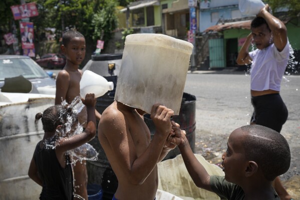 FILE - A child covers his head with a bucket on a hot day in the Los Guandules neighborhood of Santo Domingo, Dominican Republic, Monday, May 20, 2024. (AP Photo/Matias Delacroix, File)