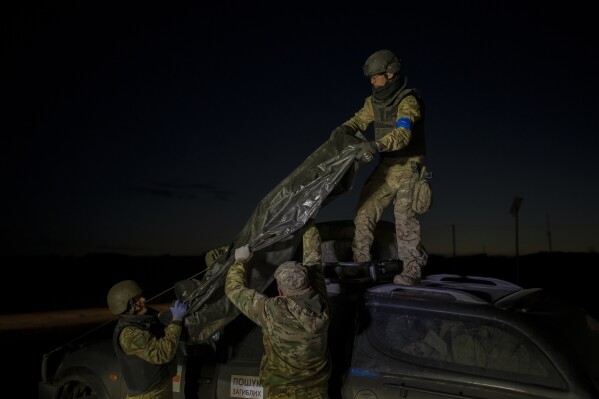 Oleksii Yukov's team members offload the bodies of Russian soldiers they've collected from the frontline in the Sloviansk region, Ukraine, Tuesday, Oct. 24, 2023. Yukov and his team retrieve bodies from the frontline to barter for Ukrainian bodies in periodic exchanges of war dead. (AP Photo/Bram Janssen)