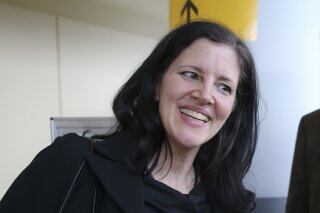 FILE - In this April 11, 2014 file photo, filmmaker Laura Poitras smiles after arriving at John F. Kennedy International Airport in New York. Poitras’ travel nightmare began a decade ago when the award-winning documentary filmmaker started getting detained at airports every time she tried to step foot back in the United States. She would be stopped without explanation more than 50 times on foreign trips and dozens of times during domestic travel. Only now is Poitras beginning to unravel the mystery, which starts on a bloody day in Baghdad in 2004. (AP Photo/John Minchillo, File)