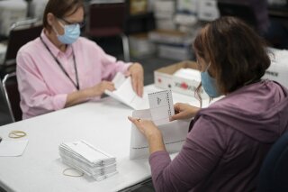 FILE - In this July 29, 2020, file photo, Lisa Finander, right, checks that each ballot has the voter's name on the ballot and mailing envelope and Laurie Mattila, left, checked that it was correct at Minneapolis Elections & Voter Services in Minneapolis. A federal judge has upheld a state court agreement that extends Minnesota's deadline for counting absentee ballots by seven days. Republicans had asked U.S. District Judge Nancy Brasel to block the seven-day extension that Democratic Secretary of State Steve Simon agreed to in state court after a citizens’ rights group cited concerns about voter safety due to the COVID-19 pandemic. But Brasel ruled late Sunday, Oct. 11, 2020, that the plaintiffs in the case — a pair of Republicans serving as electors in the presidential election — don't have standing and denied their motion for a preliminary injunction.(Glen Stubbe/Star Tribune via AP, File)