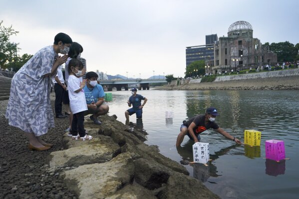 People pray as paper lanterns float along the Motoyasu River in front of the Atomic Bomb Dome, Aug. 6, 2020, in Hiroshima, western Japan. Japan marked the 75th anniversary of the atomic bombing of Hiroshima. The official lantern event was canceled to the public due to coronavirus but a small group of local representatives released some lanterns. (AP Photo/Eugene Hoshiko)