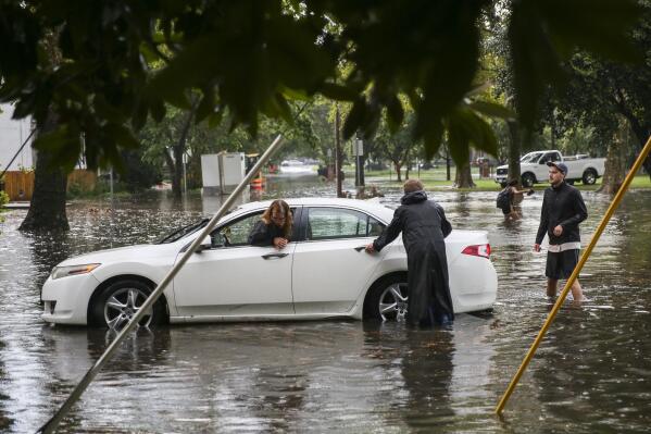 Neighbors help a stranded driver after her car got stuck after attempting to drive through high waters on West Princess Anne Road in the Ghent neighborhood of Norfolk, Va., after heavy rainfall Aug. 11, 2020. The increasing threat of sea-level rise on Virginia’s coast means that an afternoon rainstorm can strand drivers for hours and damage cars beyond repair. The city of Norfolk is trying to do something about that. Officials have partnered with the tech firm FloodMapp and the Waze traffic app to warn residents of flooded roadways in real time.  (Kristen Zeis/The Virginian-Pilot via AP)