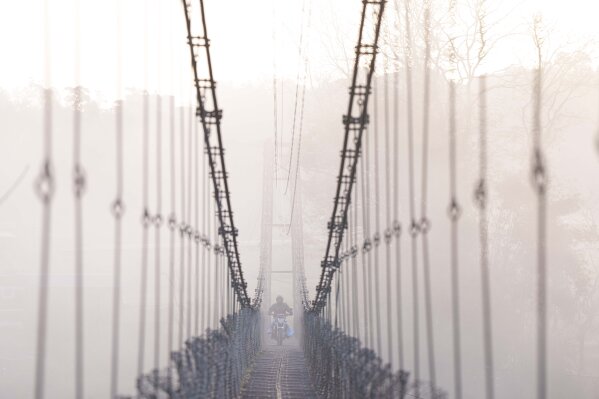 A man on a motorcycle crosses a suspension bridge over the Bagmati river in Lalitpur, Nepal, Monday, March 27, 2023. (AP Photo/Niranjan Shrestha)