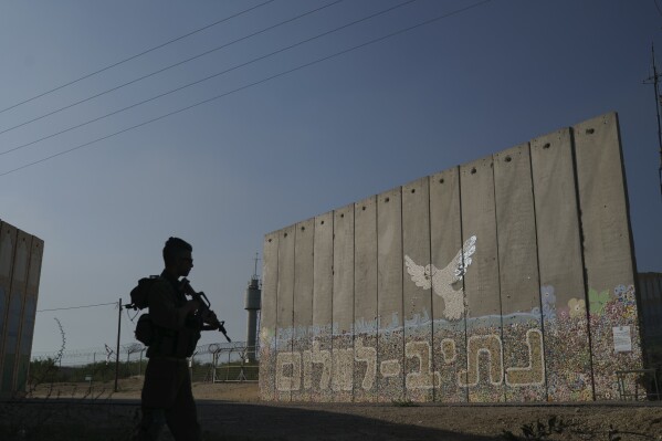A member of the Israeli forces stands near a security wall with Hebrew writing that reads "Path to Peace" at the Kibbutz Netiv Haasara, Israel, near the border with the Gaza Strip, Friday, Nov. 17, 2023. (AP Photo/Leo Correa)