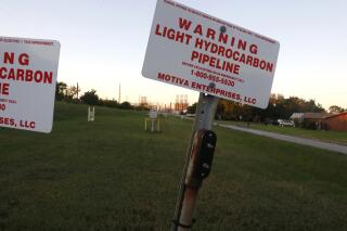 Signs mark a light hydrocarbon pipeline near a neighborhood in Port Arthur, Texas, on Wednesday, Oct. 27, 2021. The city is home to several oil refineries, including the one in the background of this photo, and is near petrochemical plants and liquid natural gas (LNG) facilities, from which natural gas is increasingly exported to other countries. (AP Photo/Martha Irvine)