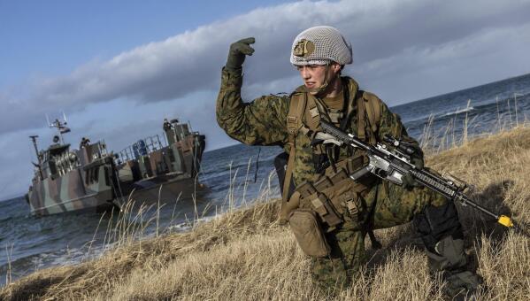 In this image provided by the North Atlantic Treaty Organization, a U.S. marine waves his troops onward after using Dutch landing craft to land near Sandstrand, Norway, March 21, 2022, during the Exercise Cold Response 22. (NATO via AP)