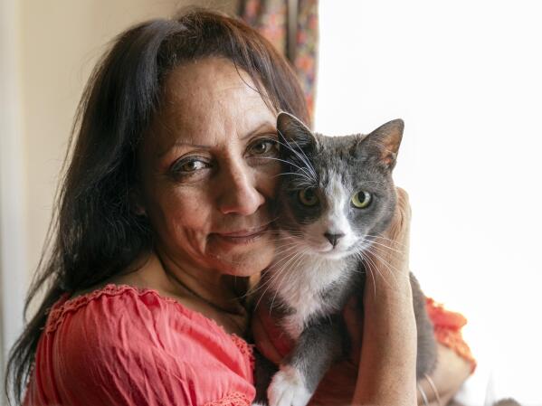 In this Wednesday, June 30, 2021, photo Veronica Perez hugs her cat, Brooklyn, at her new home at a Homekey site in Los Angeles.  She took residence in one of 6,000 new units built statewide over the last year as part of Project Homekey. The California program started in June 2020 is re-purposing vacant hotels, motels and other unused properties as permanent supportive housing for the homeless.  (AP Photo/Damian Dovarganes)