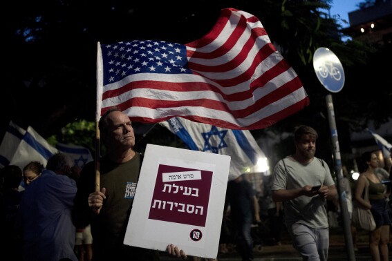 A man carries the U.S. flag with a placard reading, "horror movie for the sake of reasonableness," as Israelis march in support of the judicial system during a protest against the plans by Prime Minister Benjamin Netanyahu's government to overhaul it, in Tel Aviv, Israel, Wednesday, Aug. 2, 2023. (AP Photo/Maya Alleruzzo)